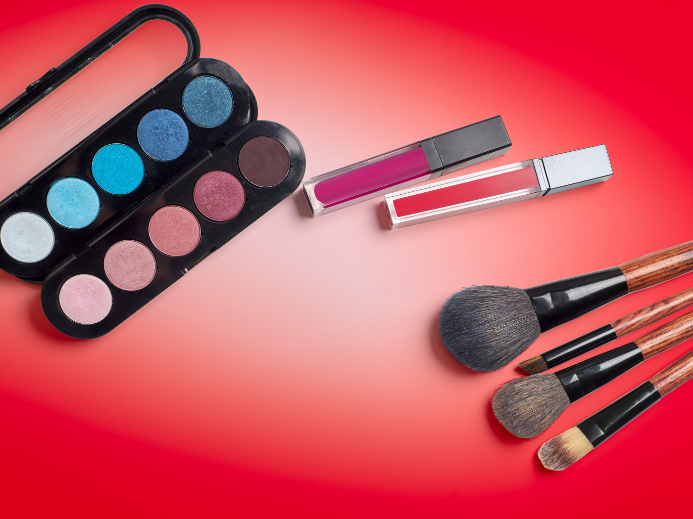 Блеск для губ, тени и кисточки на красном фоне