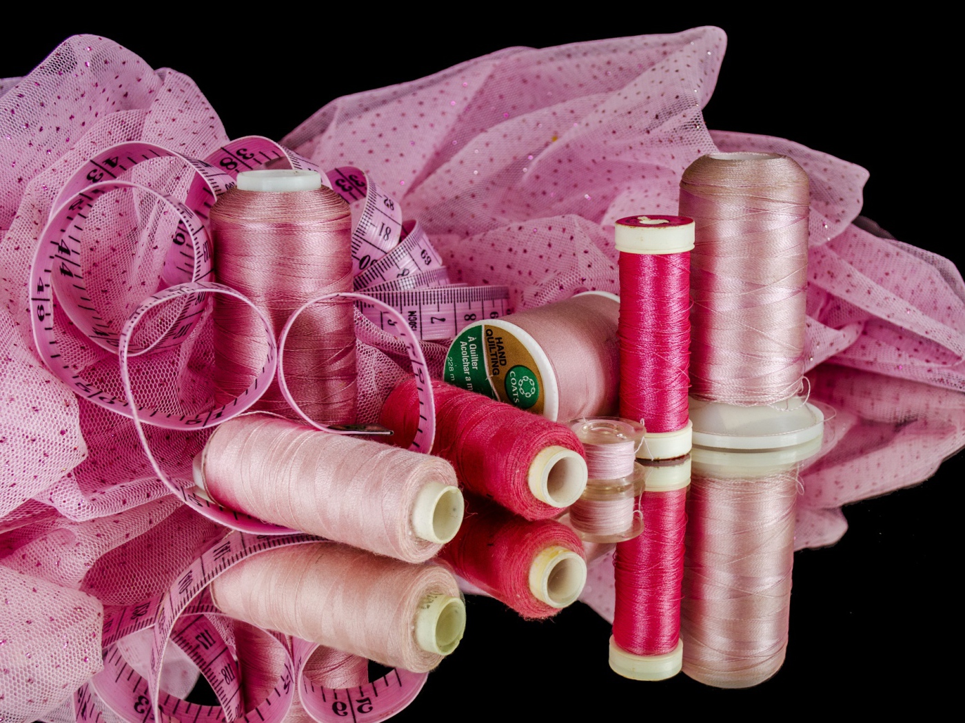 Розовые нитки с сантиметром и тканью на черном фоне 