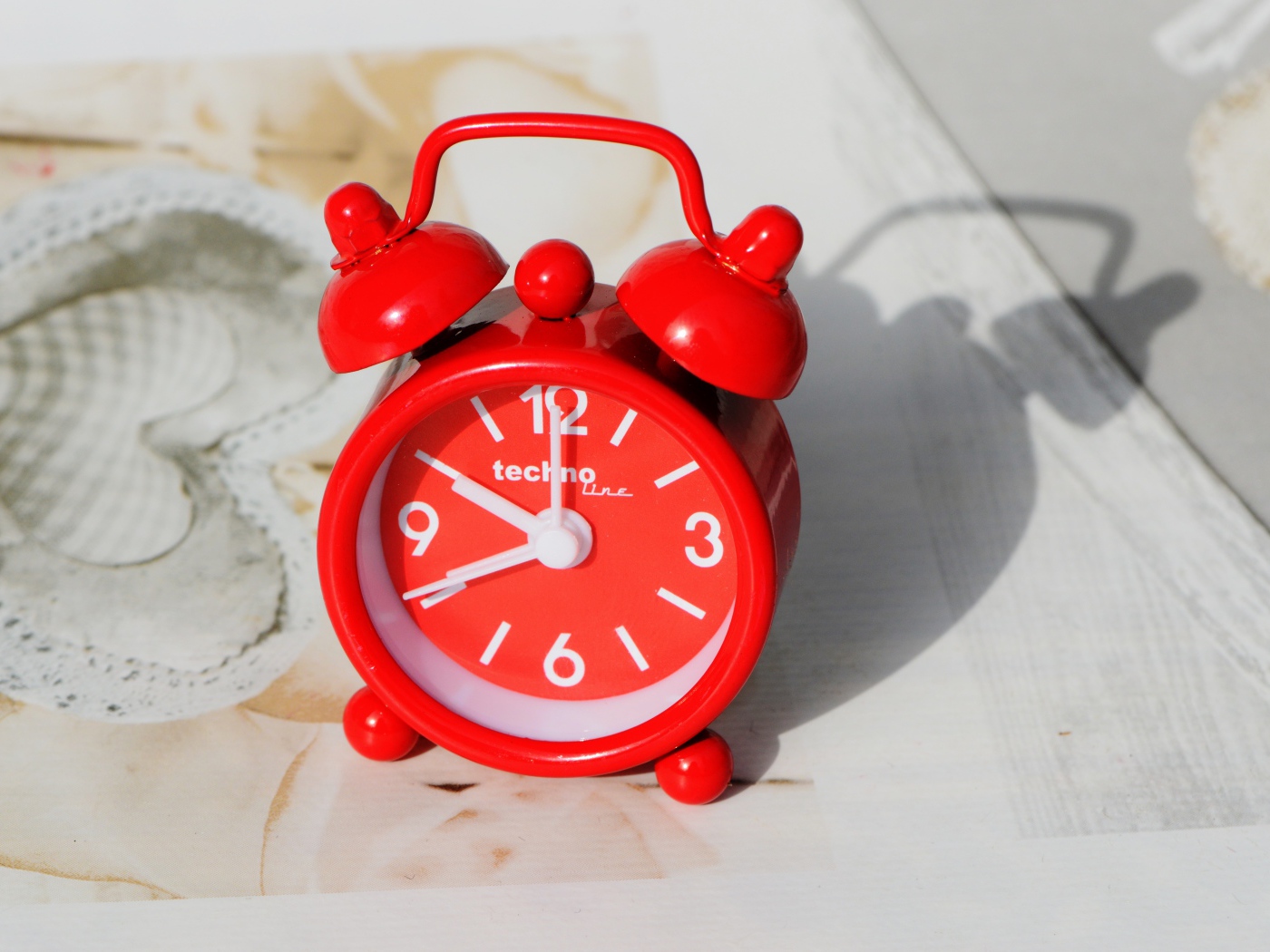 Маленький красный будильник стоит на столе 