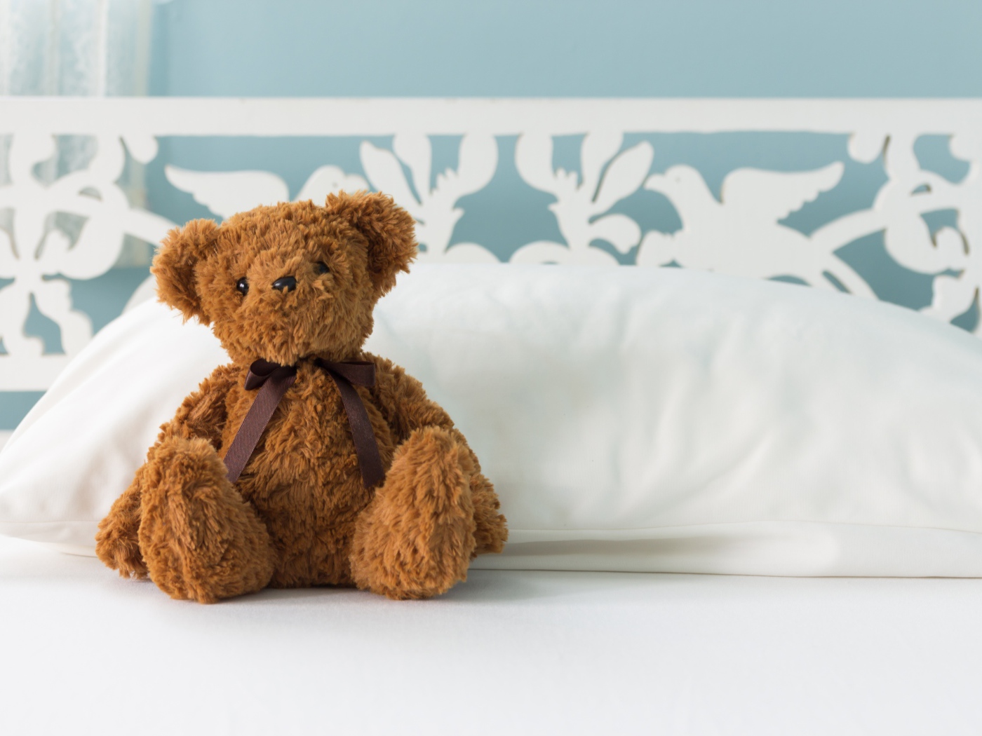 Игрушечный медвежонок сидит на белой постели