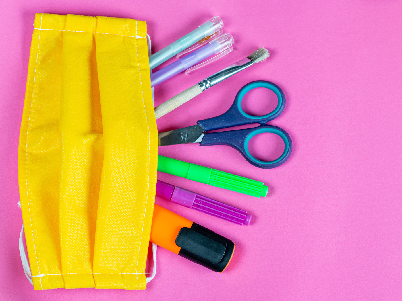 Желтая медицинская маска с ручками и ножницами на  розовом фоне