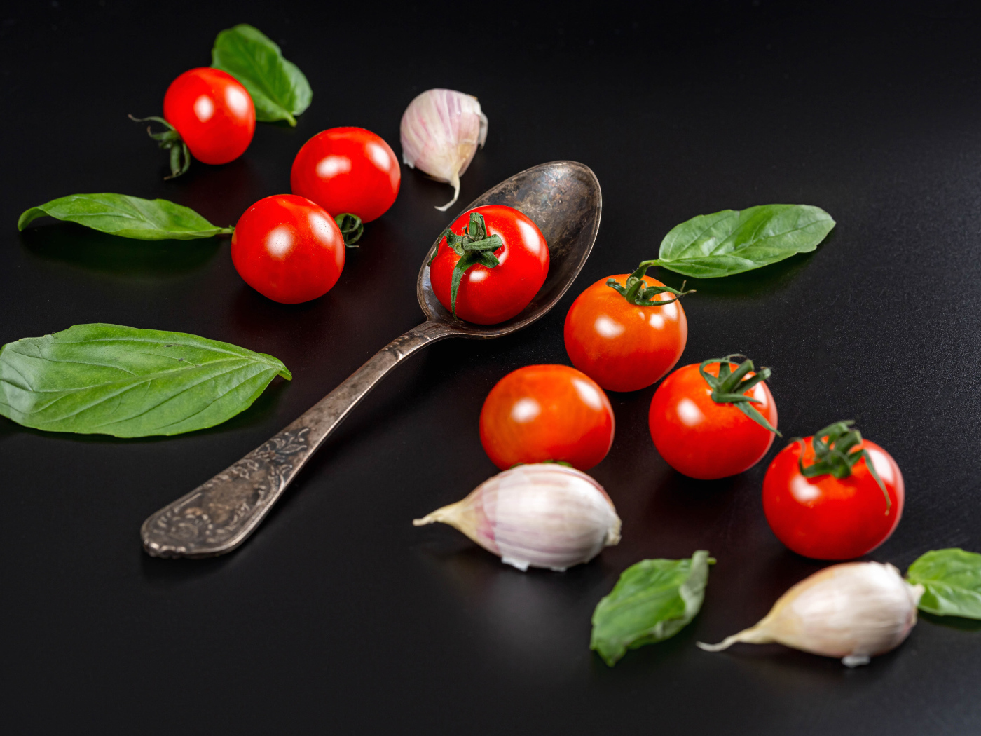 Красные помидоры с чесноком и листьями базилика на столе 