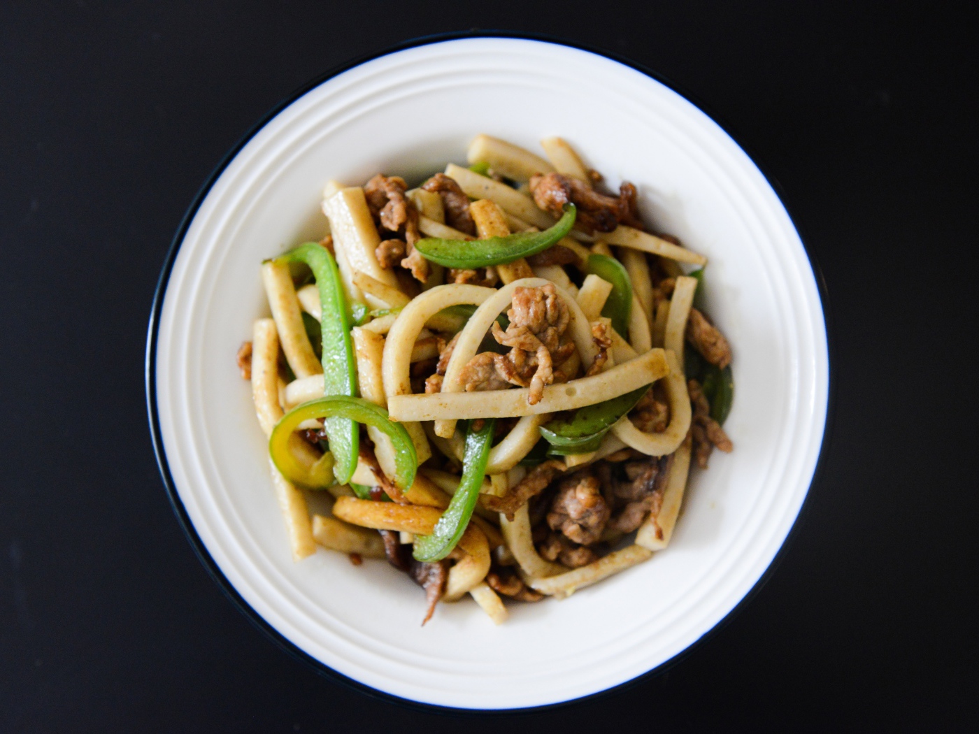 Салат с мясом в белой тарелке на черном фоне