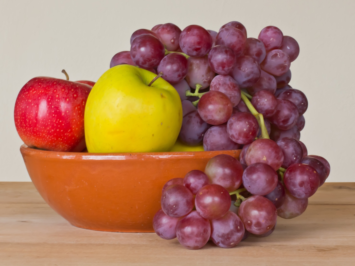 Яблоки и розовый виноград в тарелке на столе 