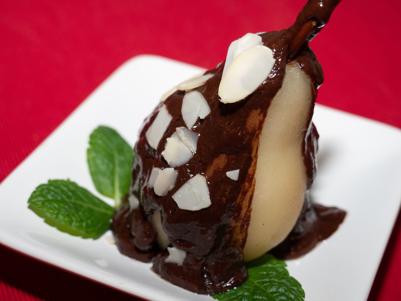 Pear on a white plate with chocolate on a red background