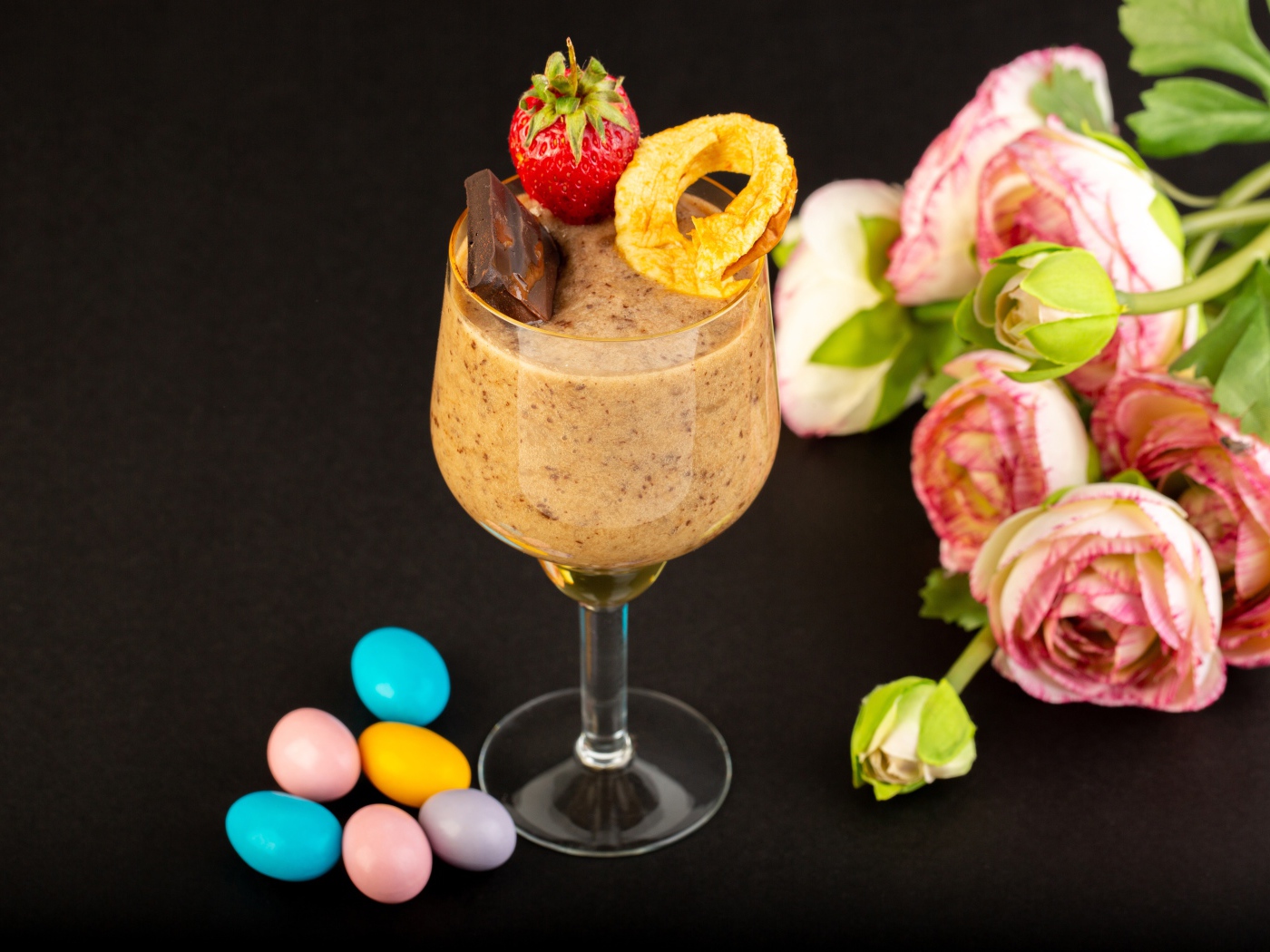 Коктейль с конфетами и букетом лютиков на черном столе