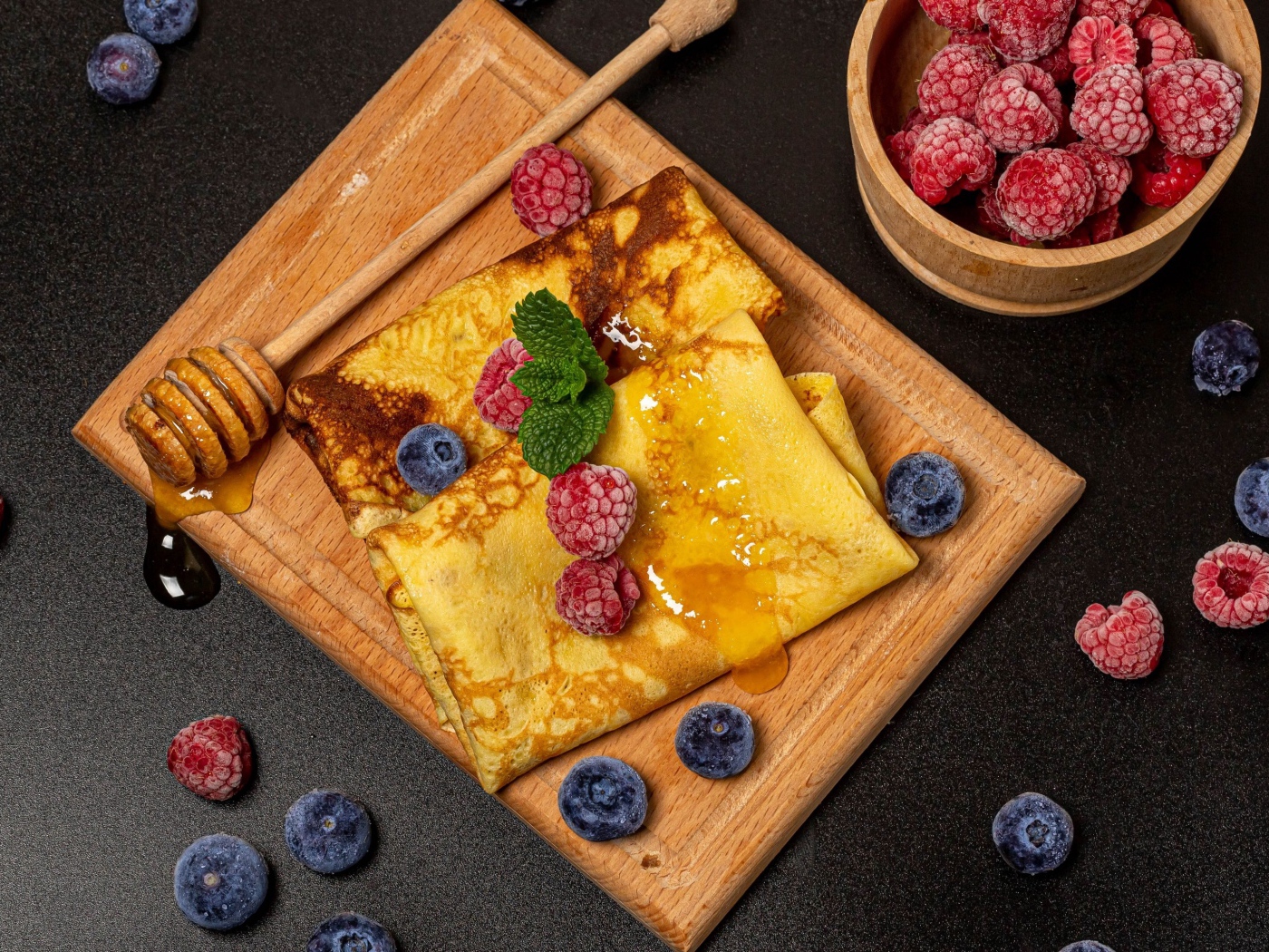 Блины с медом и ягодами черники и малины на черном столе 