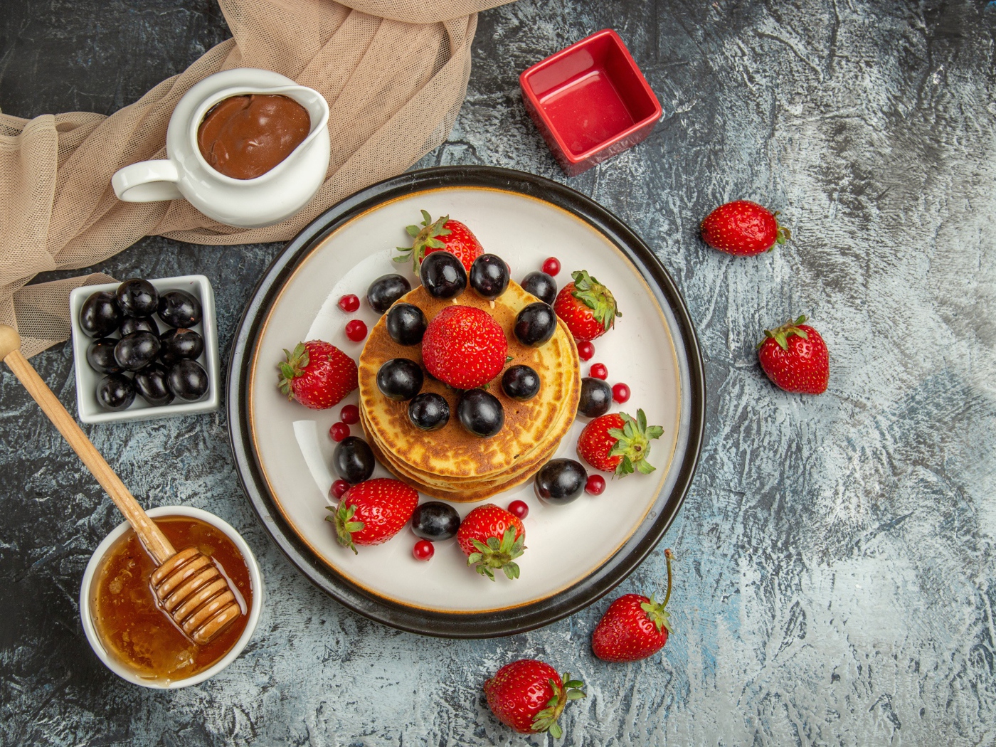 Оладьи с ягодами клубники и винограда на столе с медом