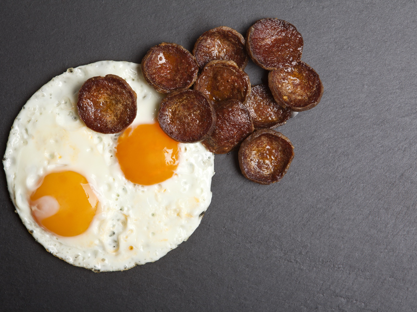 Жареная колбаса с яичницей глазуньей на сером столе 