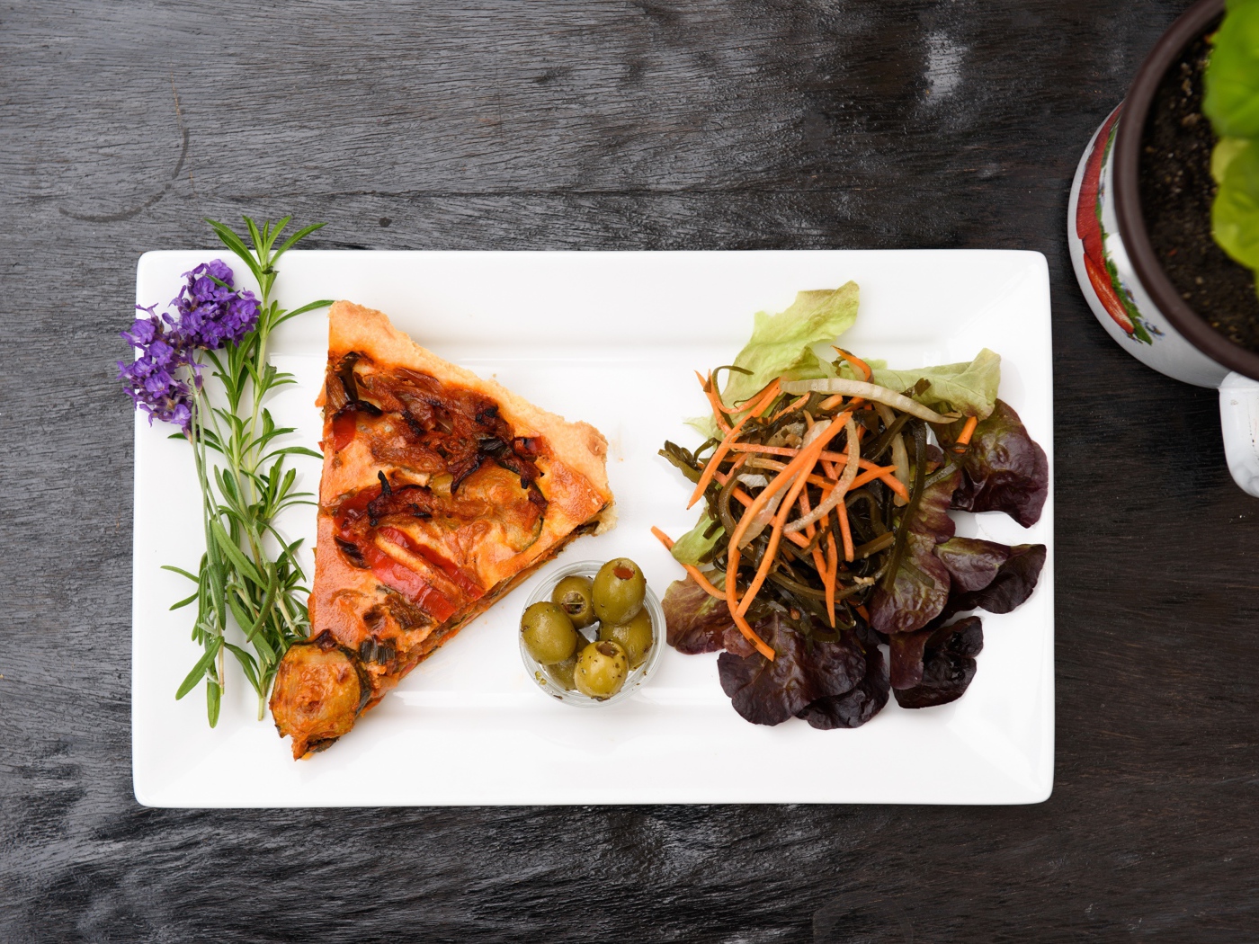 Кусок пиццы с салатом и оливками на белой тарелке