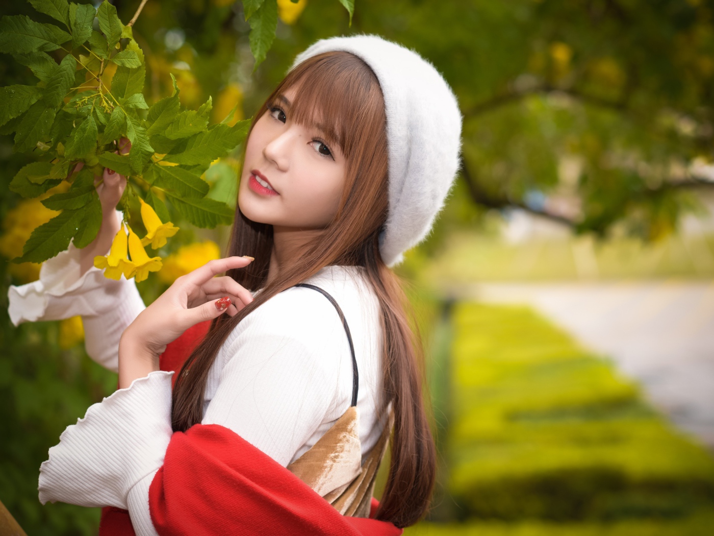 A girl in a beret stands by a bush with yellow flowers