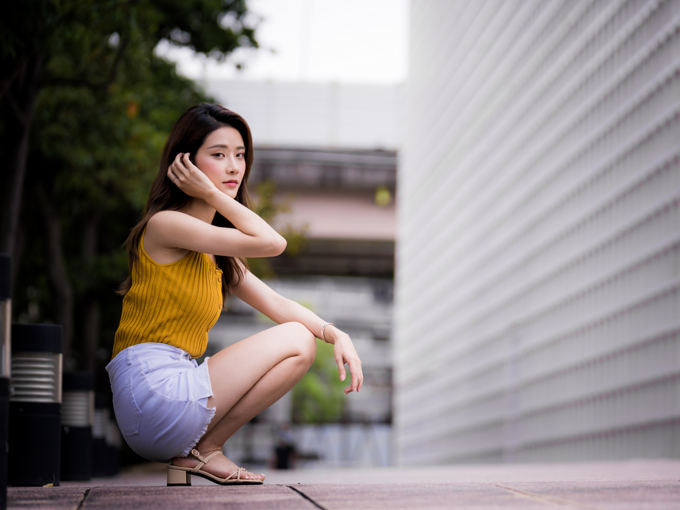 Девушка азиатка сидит на корточках у стены