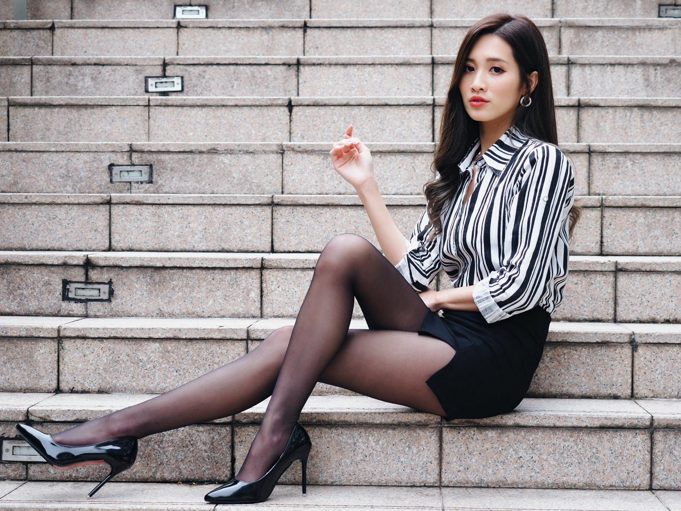 Красивая девушка азиатка в юбке сидит на ступеньках