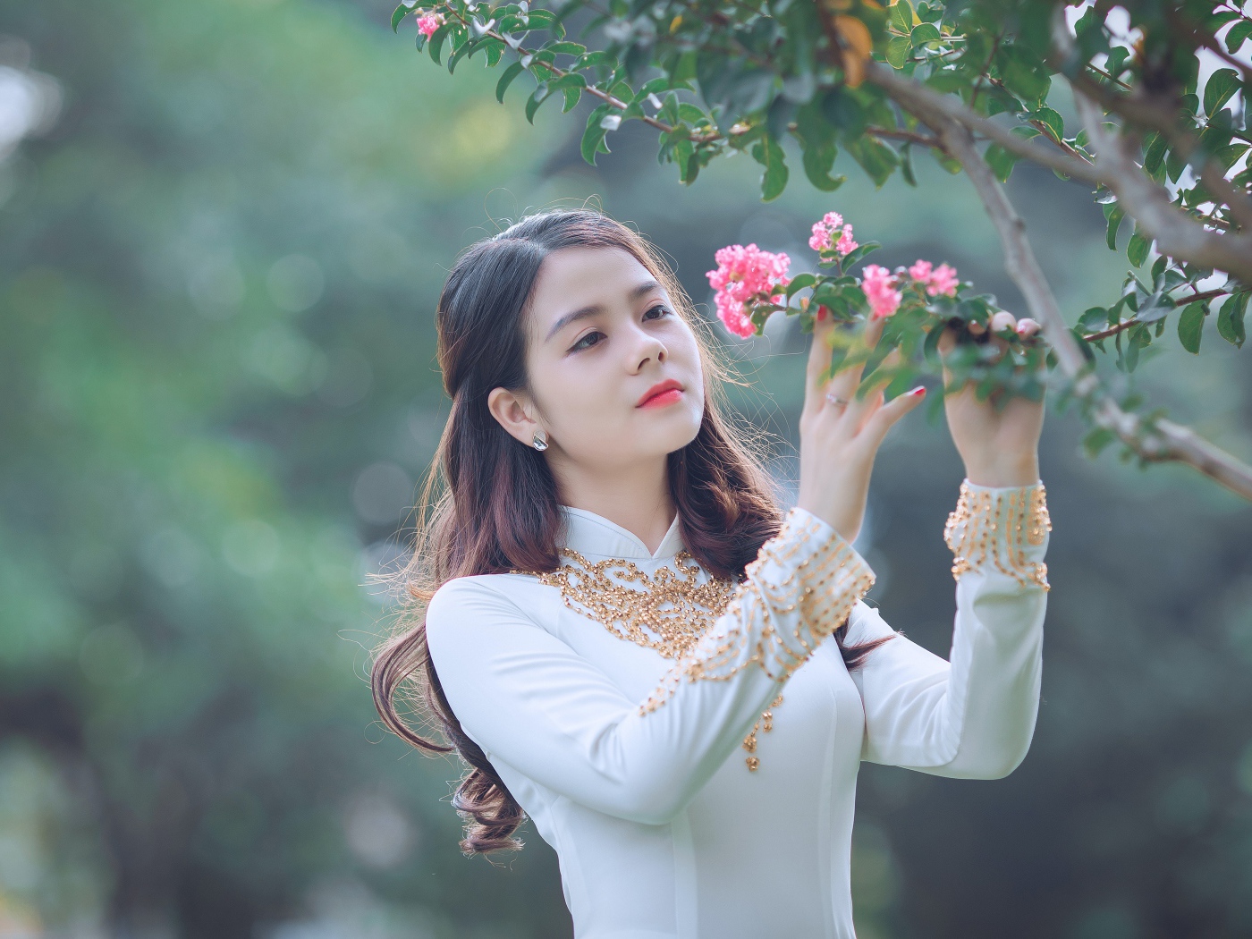 Красивая азиатка в белом платье у ветки с розовыми цветами