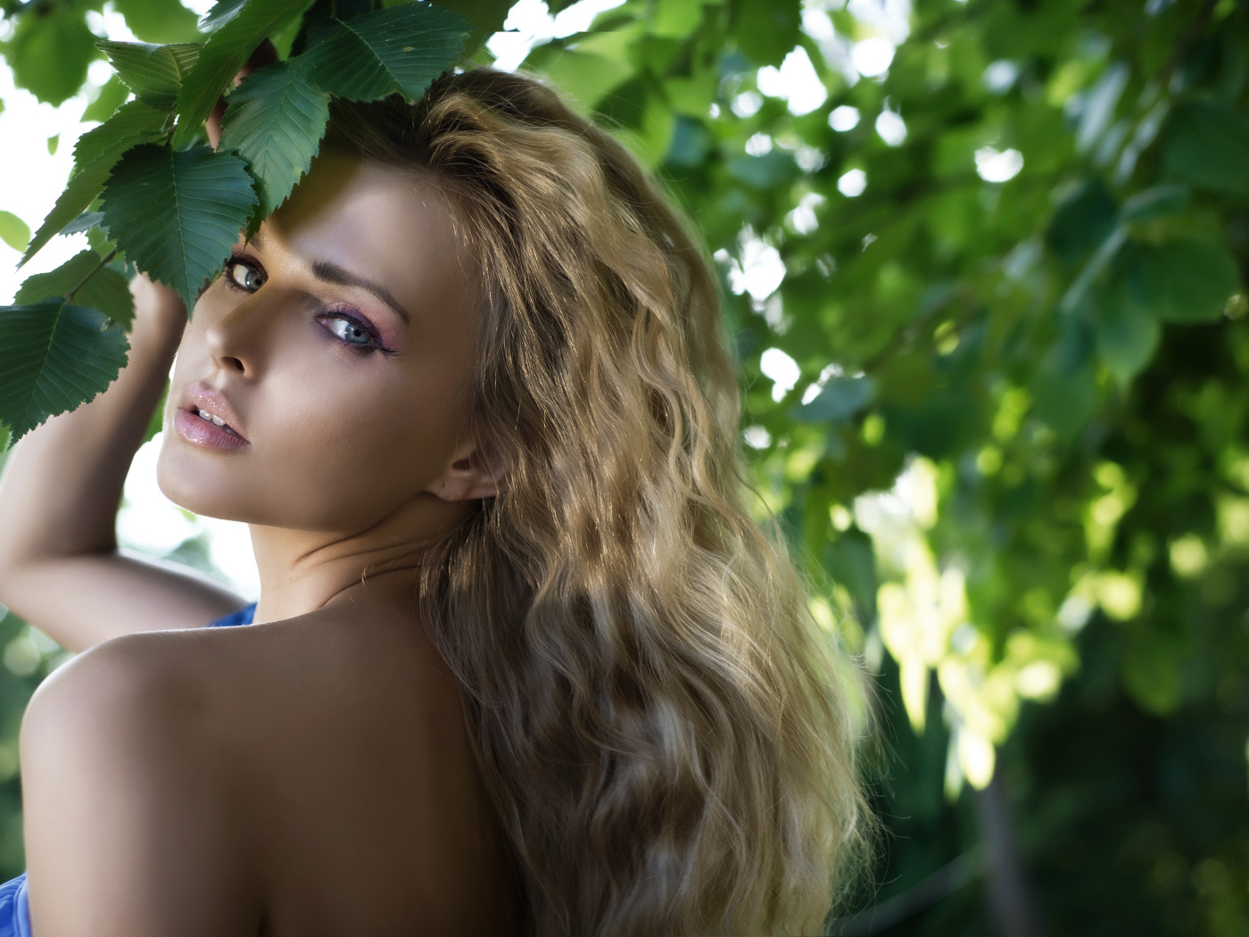 Красивая голубоглазая блондинка у ветки с зелеными листьями