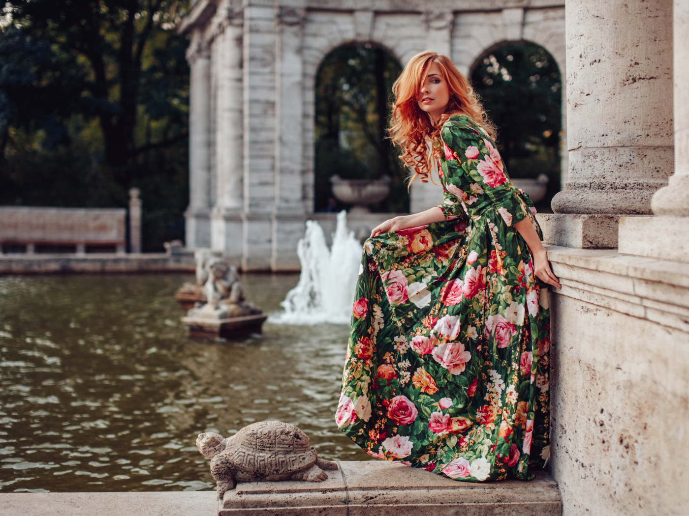 Девушка в красивом цветастом платье у пруда в парке 