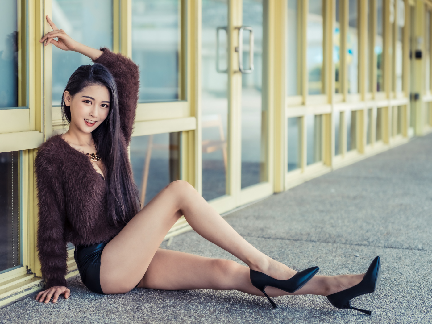 Девушка в свитере сидит у стеклянной стены 