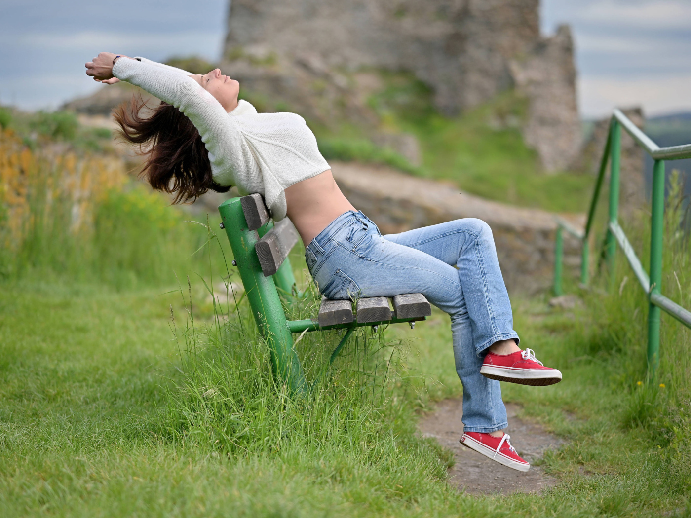 Девушка в синих джинсах сидит на лавке 