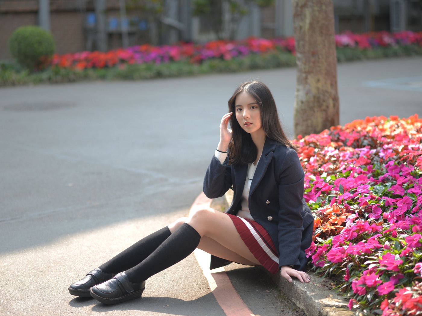 Девушка школьница сидит на земле у клумбы 