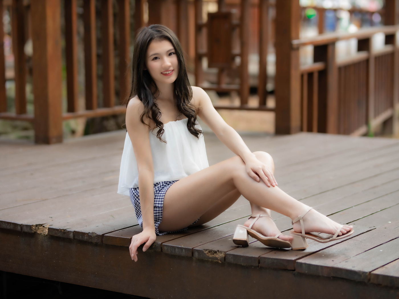 Улыбающаяся девушка азиатка сидит на мосту 