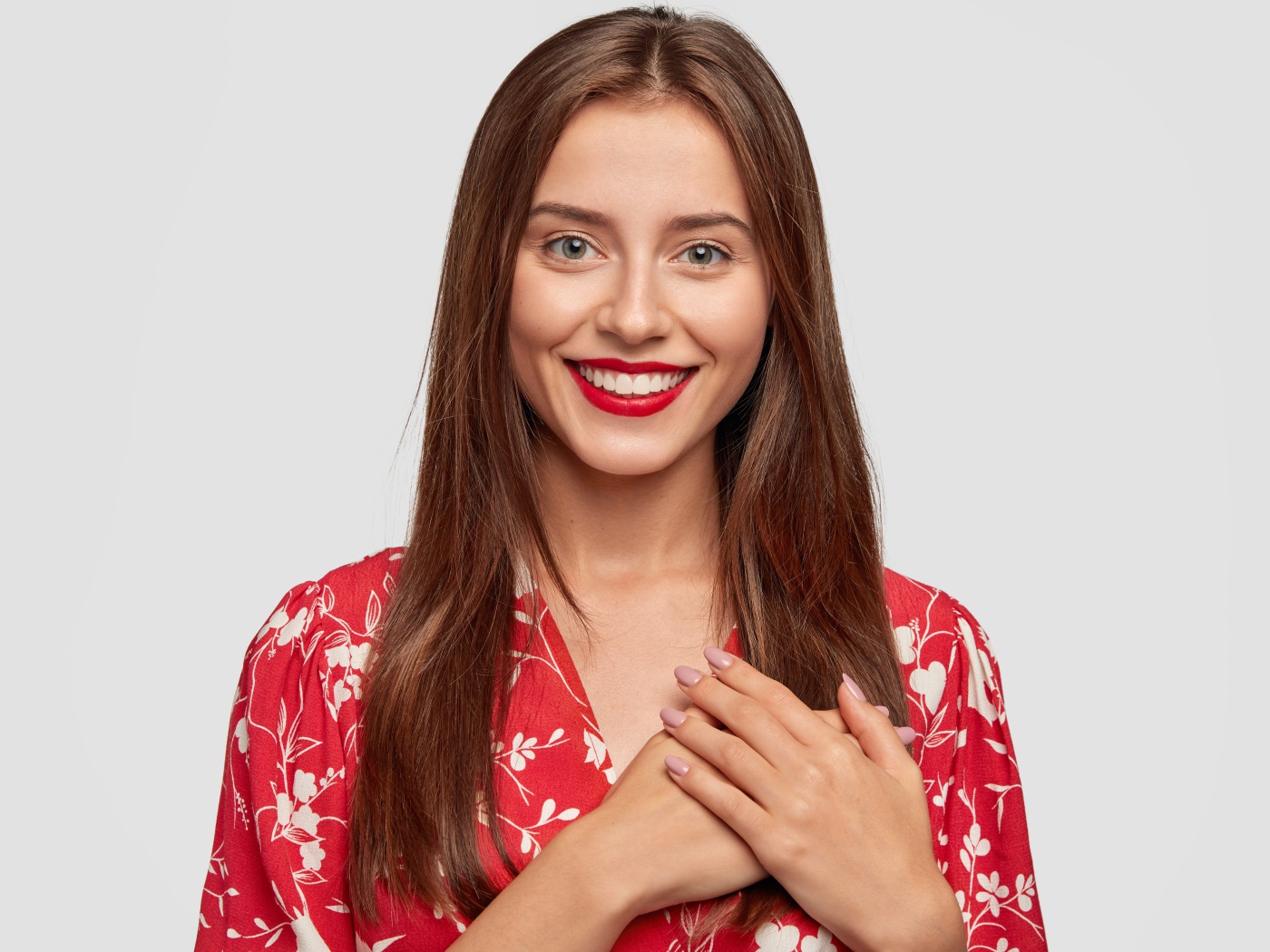 Улыбающаяся девушка с руками на сердце на сером фоне