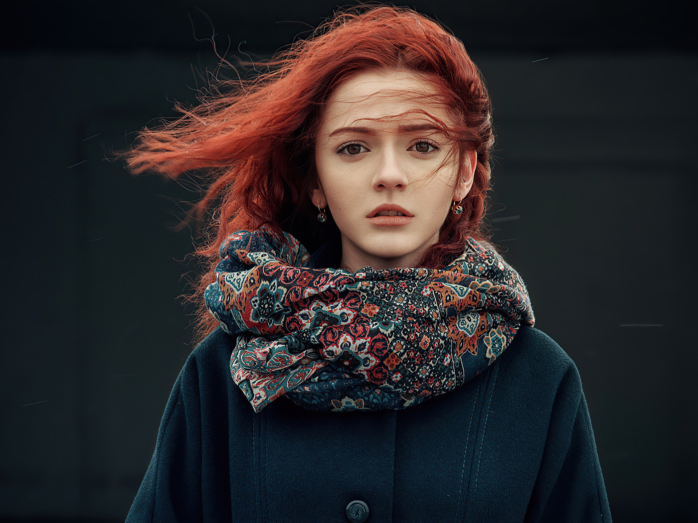 Ветер развивает волосы рыжеволосой девушки в пальто