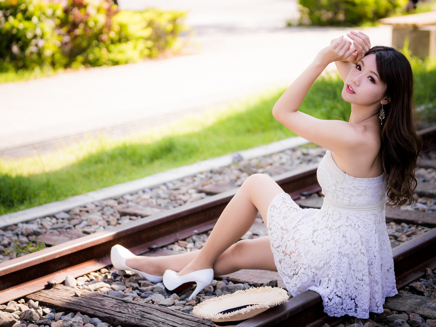 Молодая азиатка в белом платье сидит на рельсах 