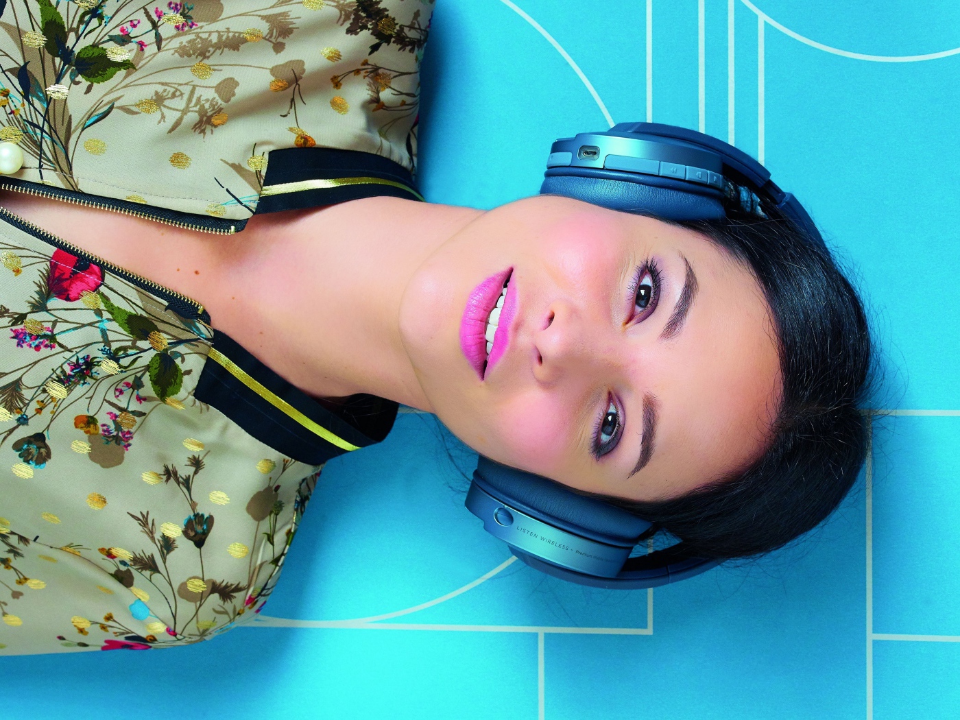 Молодая женщина в наушниках лежит на голубом полу