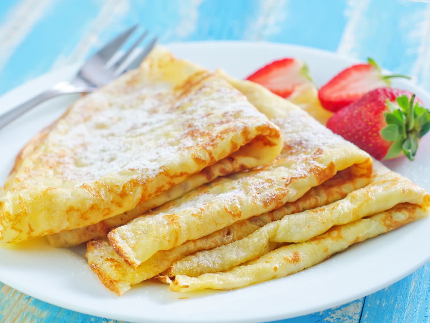 Румяные тонкие блинчики на тарелке с клубникой 