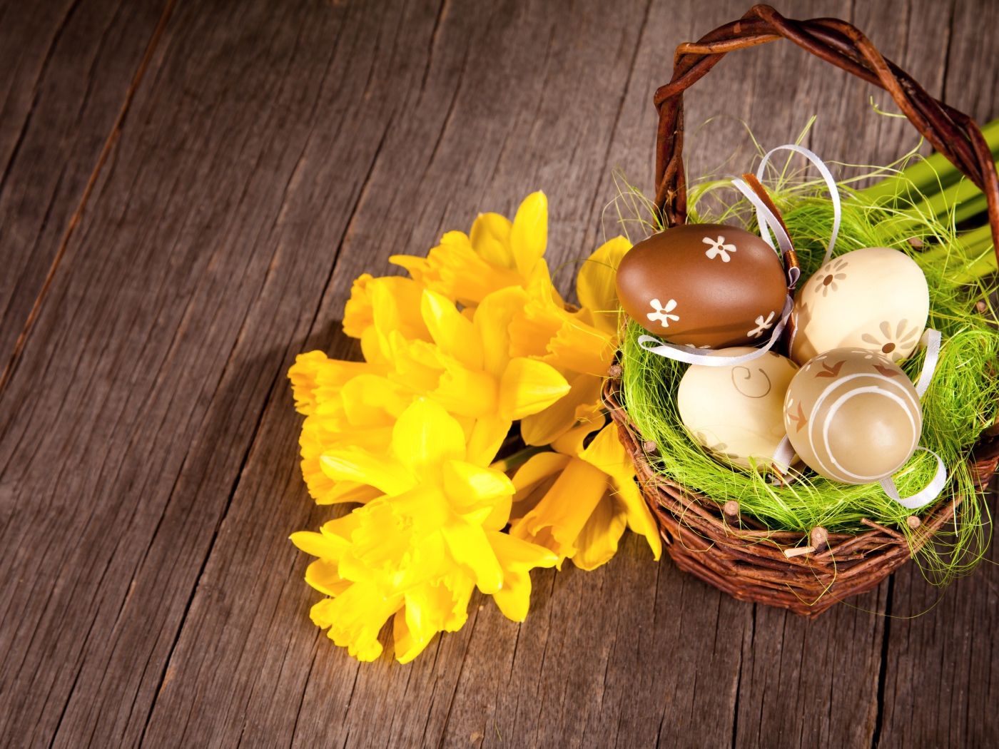 Корзина с крашеными пасхальными яйцами на столе с букетом нарциссов