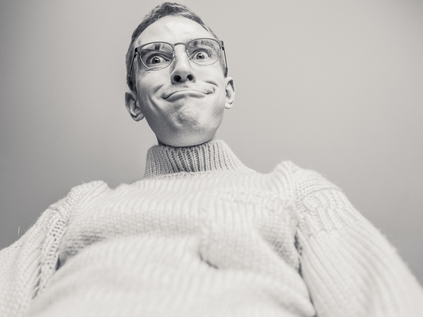 Мужчина в очках корчит лицо на сером фоне