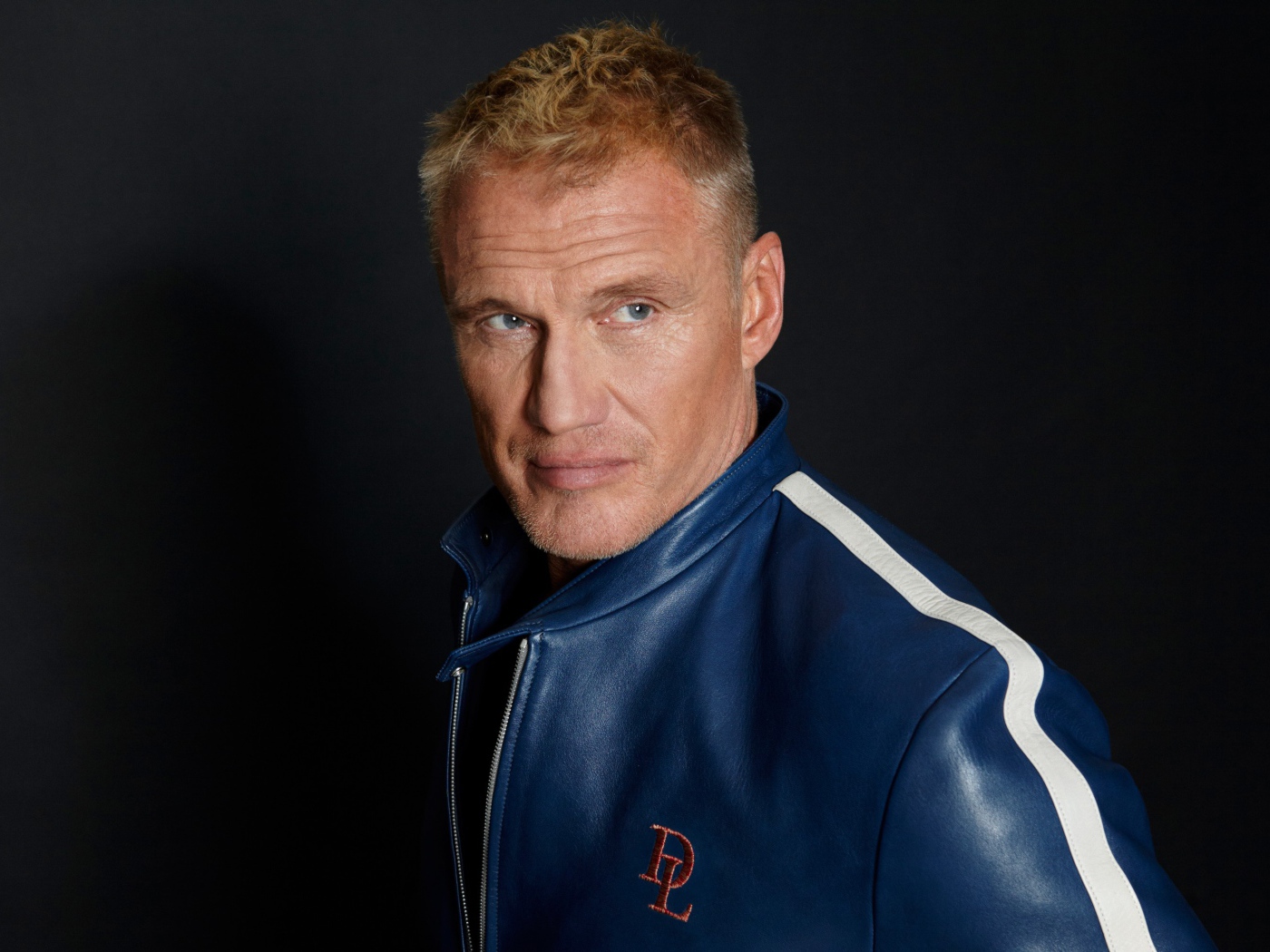 Актер Дольф Лундгрен в куртке на фоне  серой стены