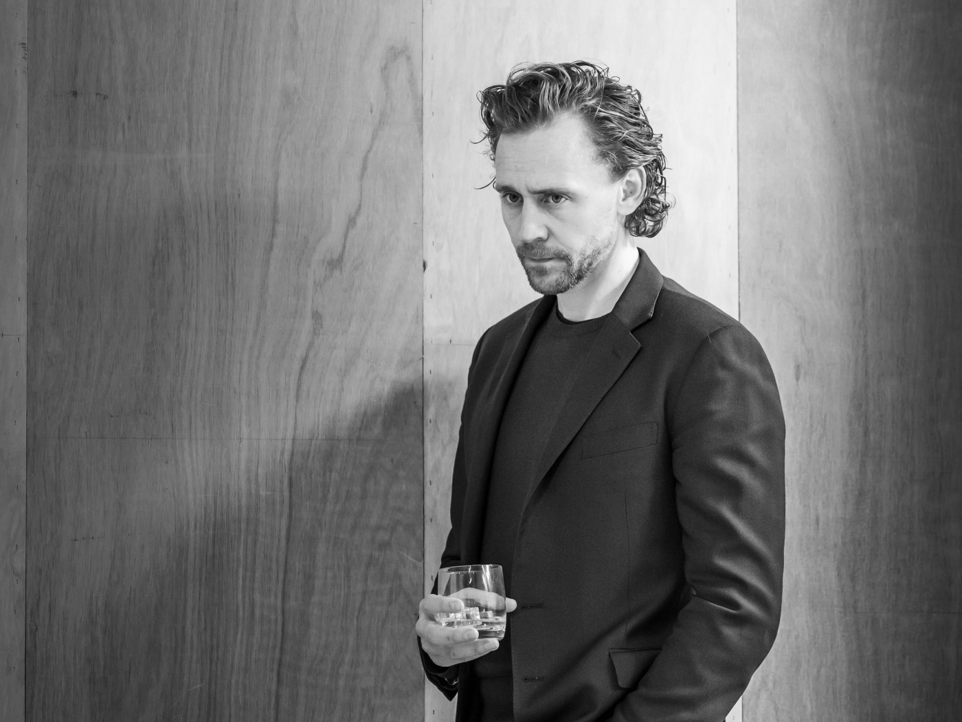 Актер Том Хиддлстон с бокалом в руке на фоне стены