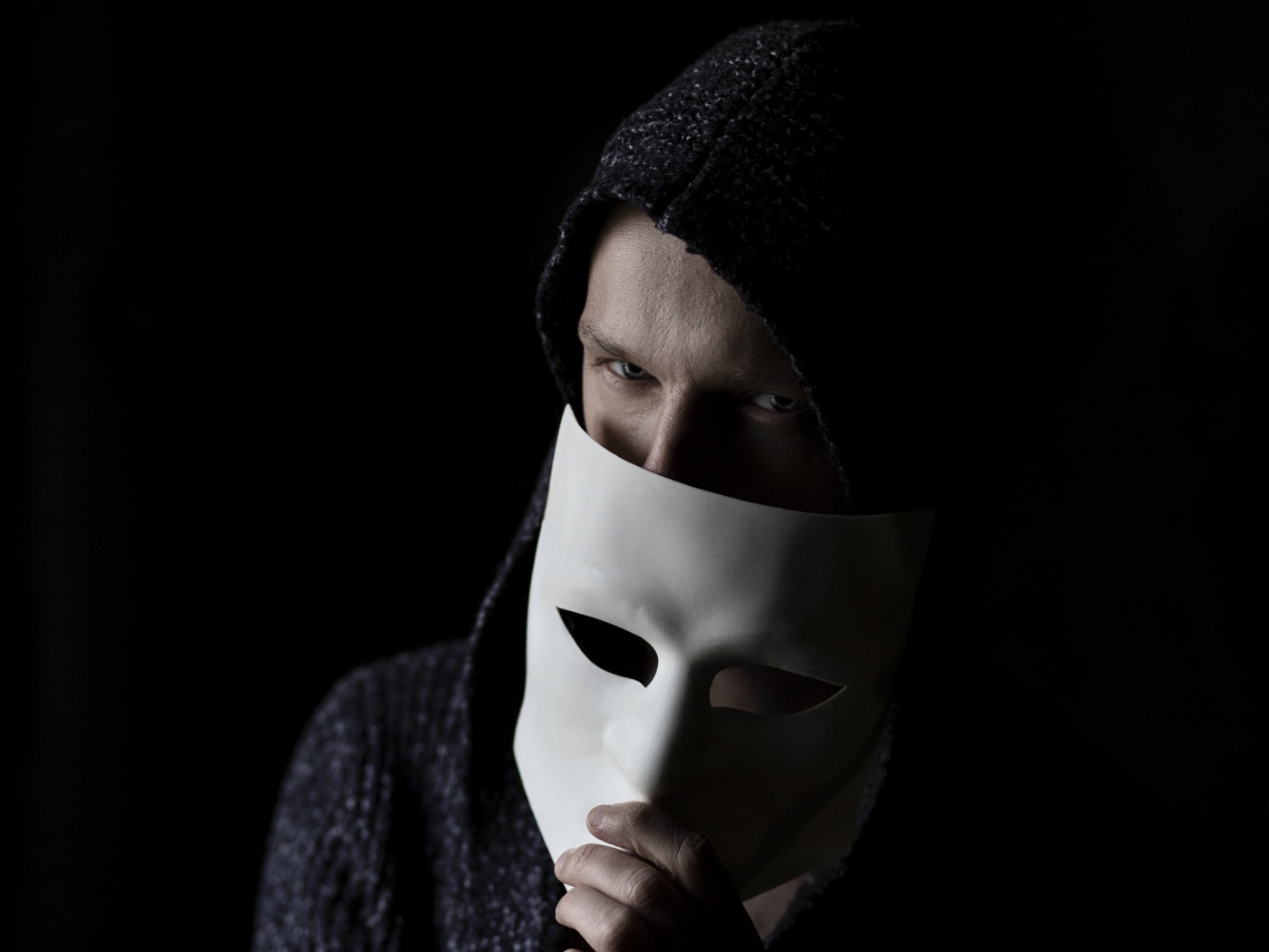 Мужчина прикрывает лицо белой маской на черном фоне