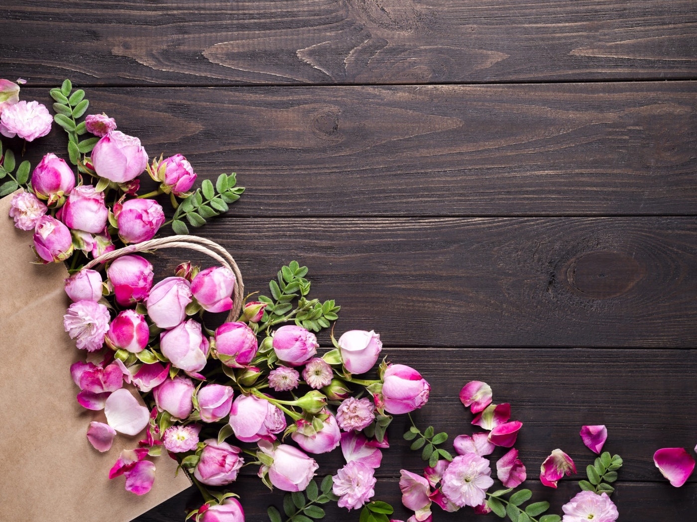 Цветки розовой розы с бумажным пакетом  на деревянном фоне