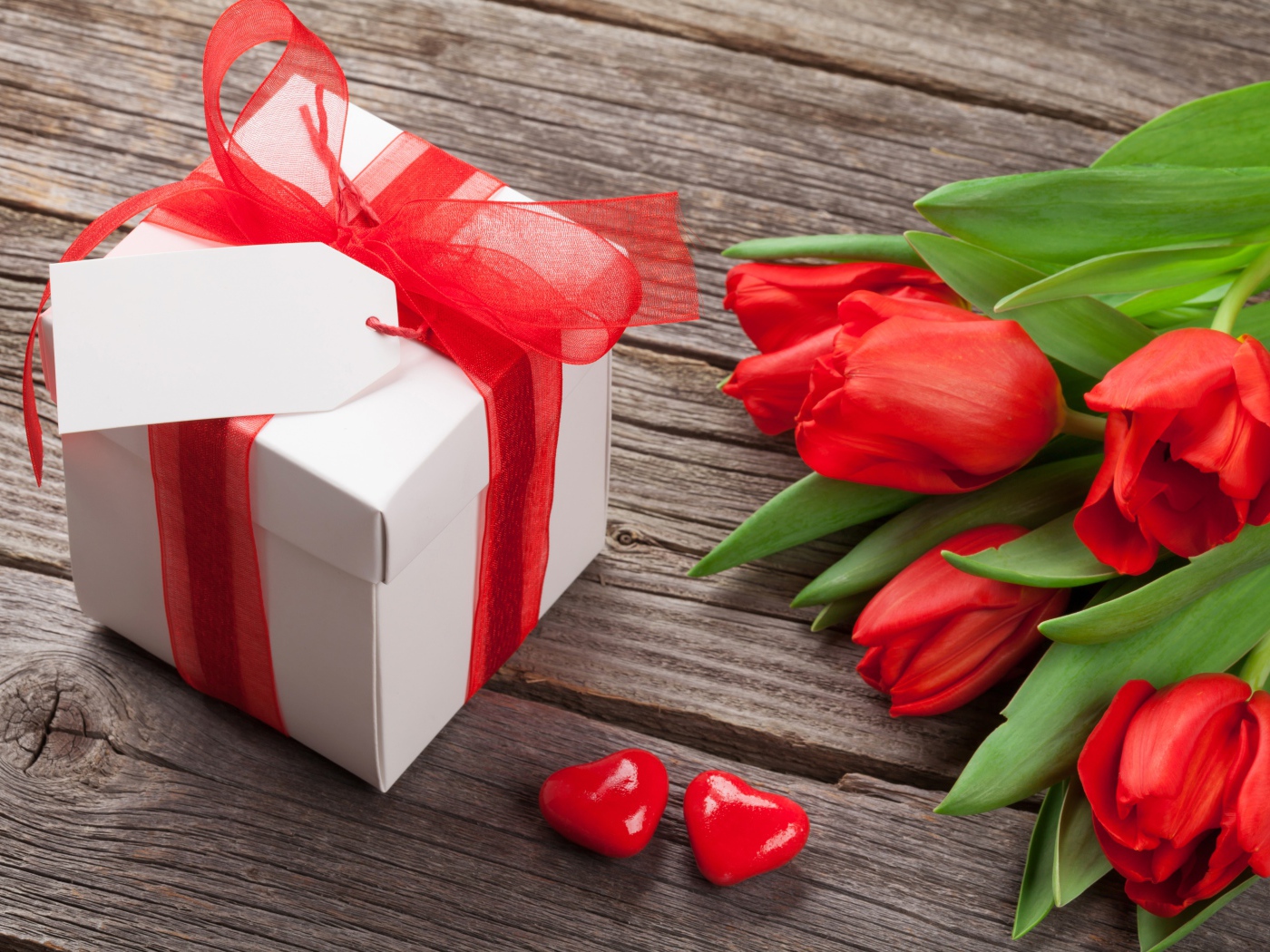 Красные тюльпаны с большим подарком на деревянном столе 
