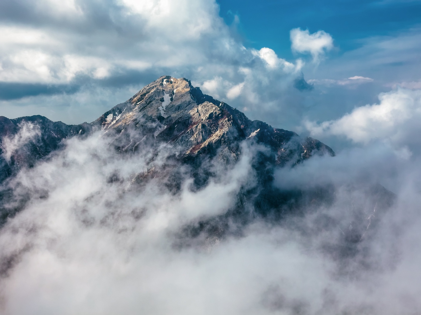 Большая высокая гора в густых белых облаках