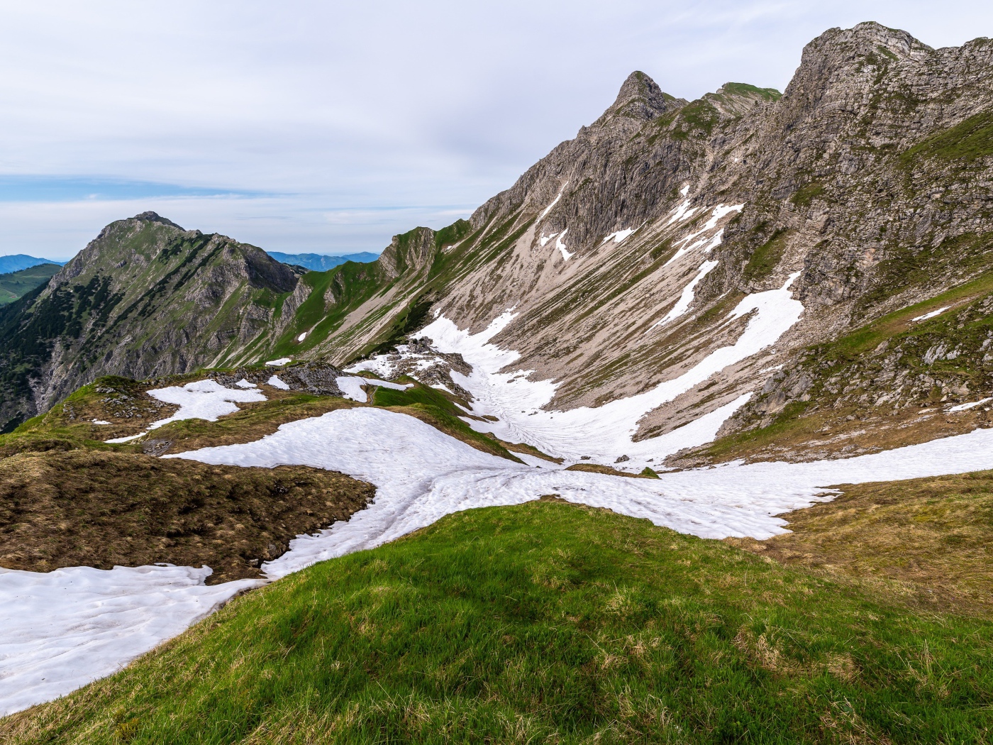 Снег на склонах горы с зеленой травой 