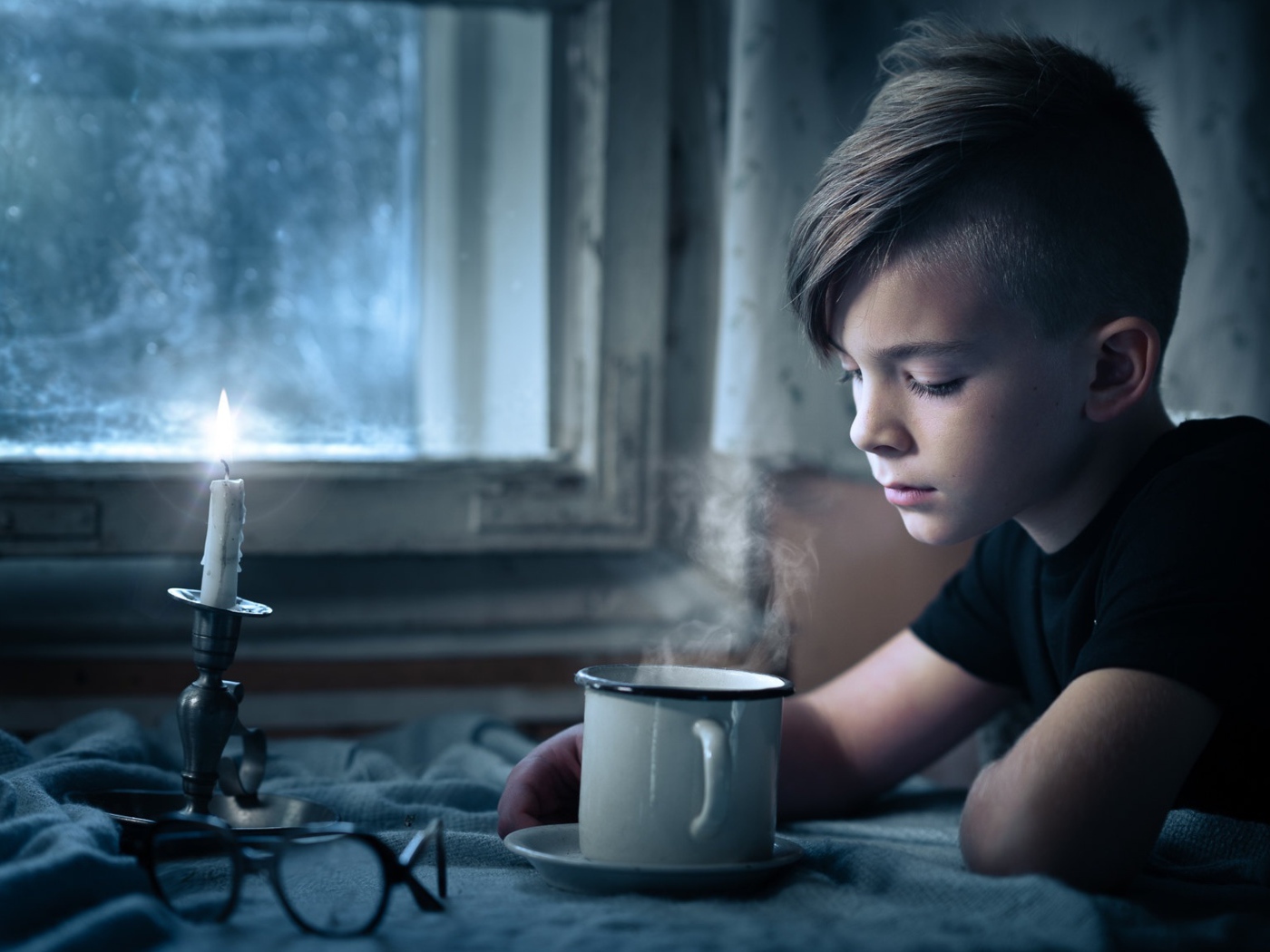 Маленький мальчик сидит за столом при свете свечи 