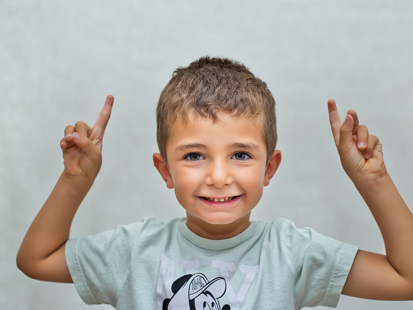 Маленький мальчик поднял руки вверх на сером фоне