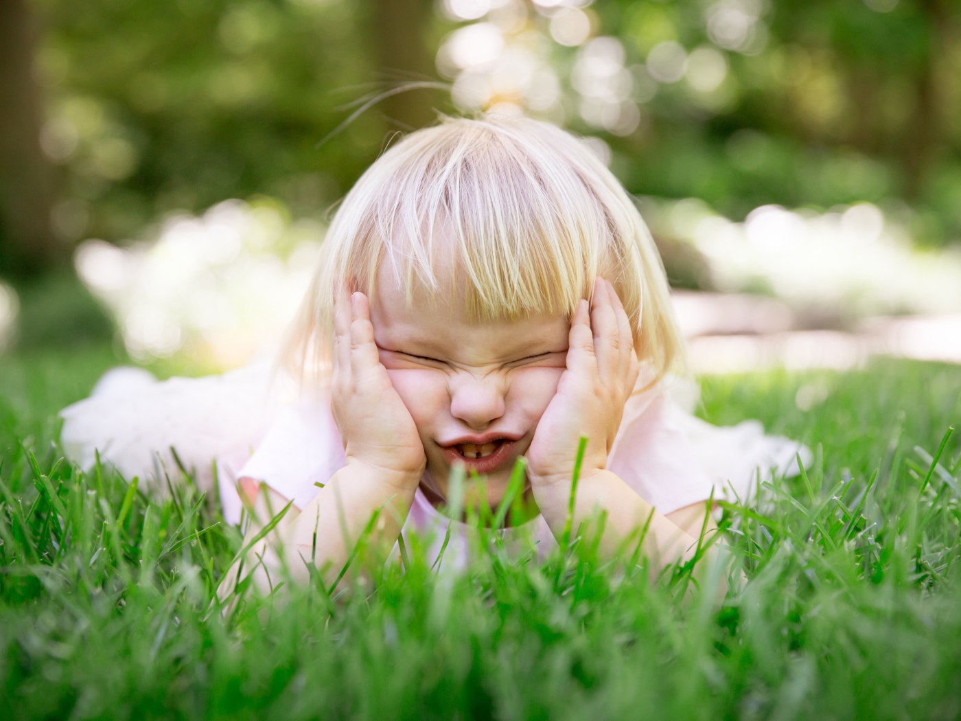 Маленькая смешная девочка лежит на зеленой траве 