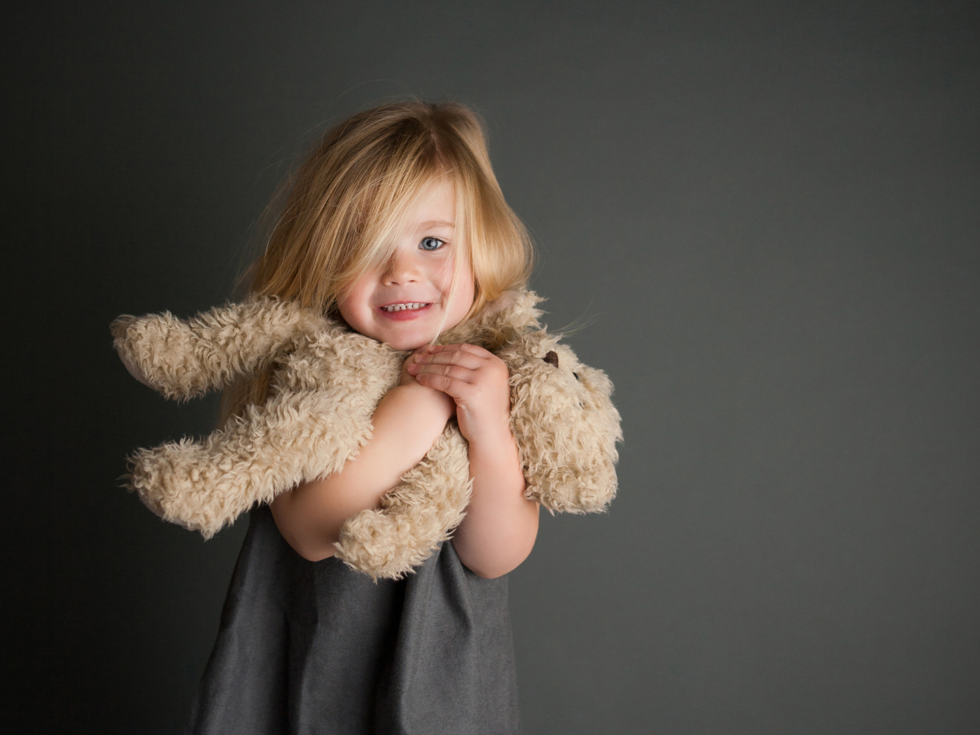 Маленькая девочка с игрушечным медвежонком в руках  на сером фоне 
