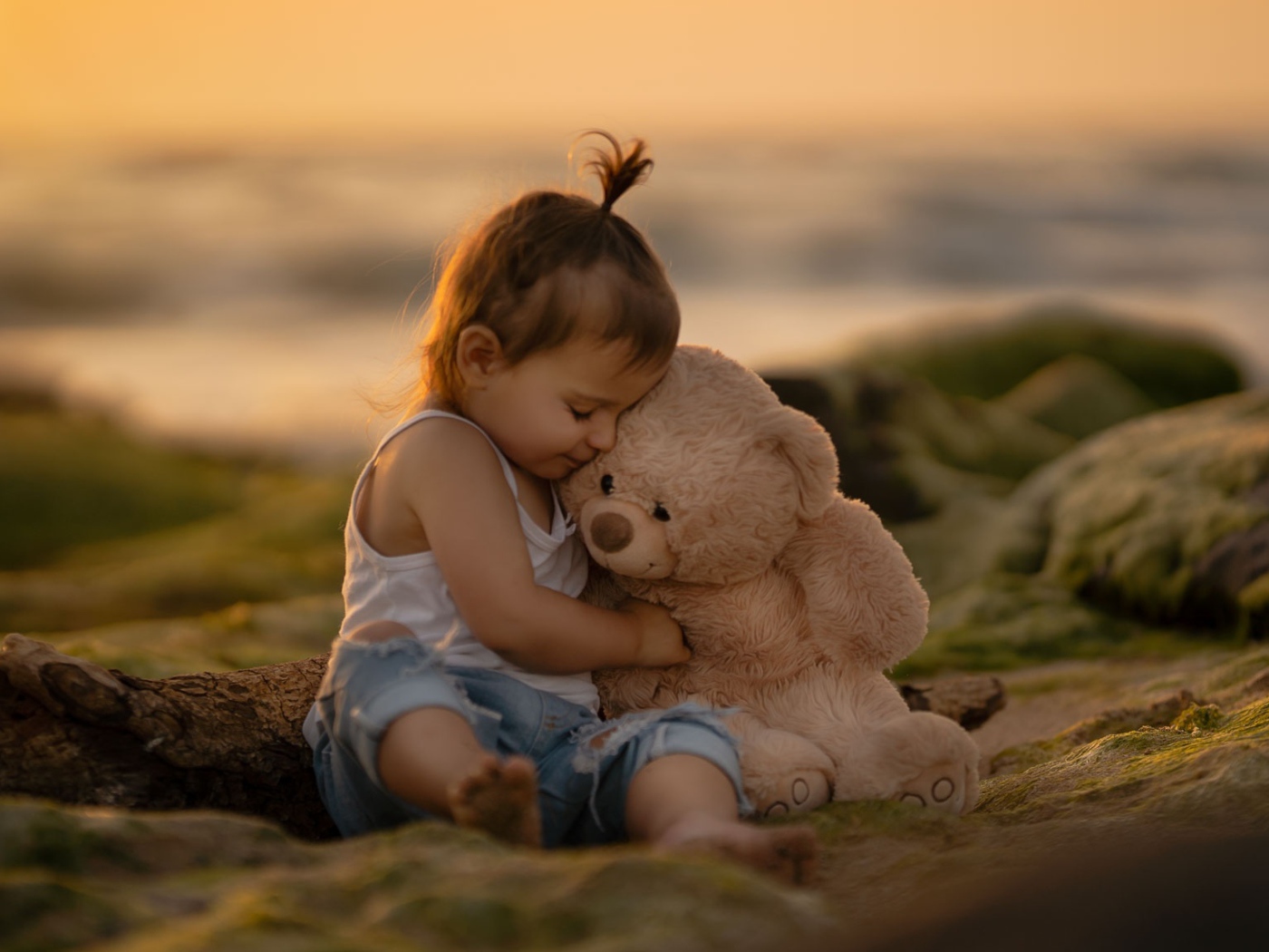 Маленькая девочка с игрушечным медведем сидит на камне