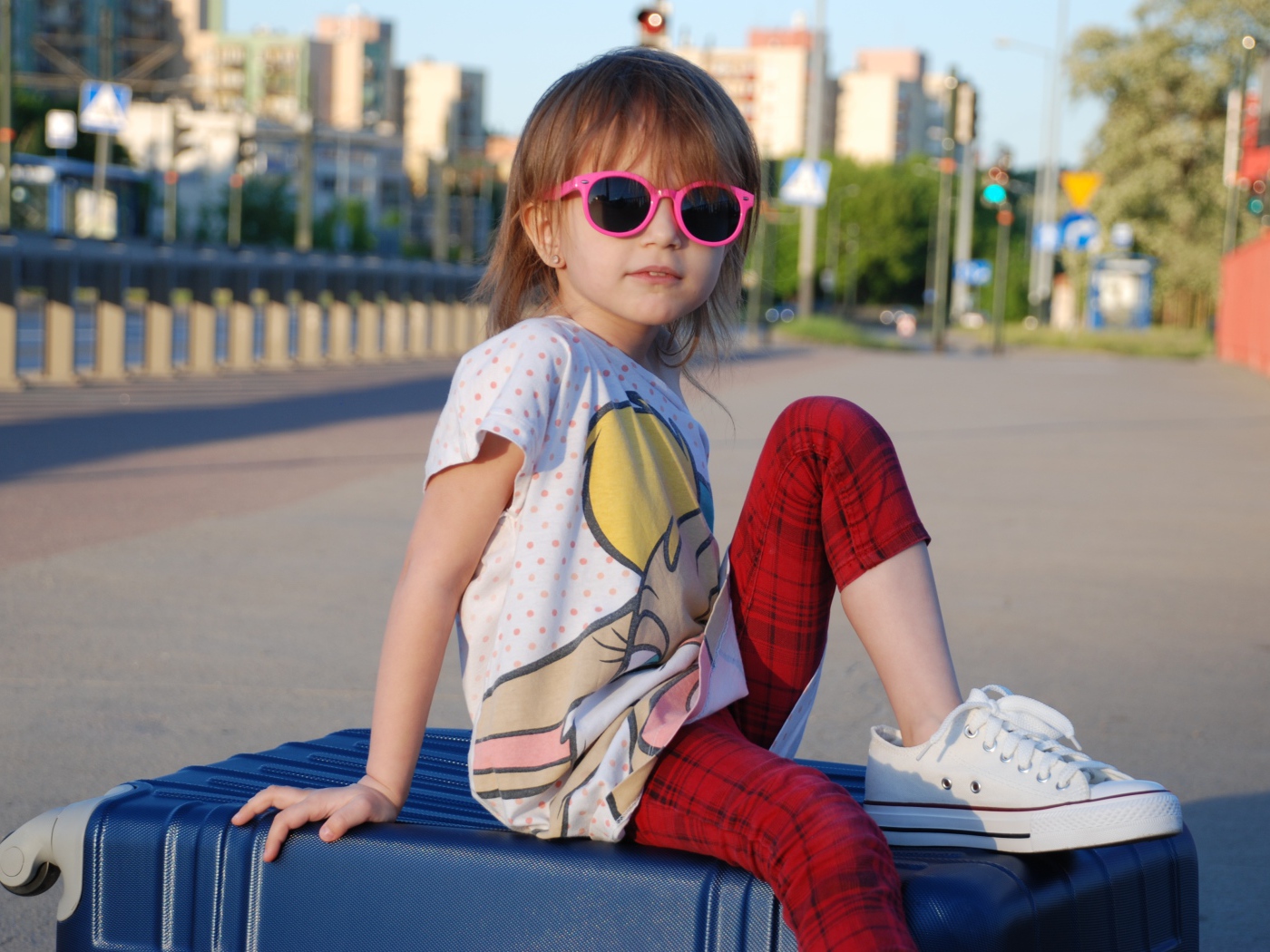 Маленькая девочка в очках сидит на чемодане