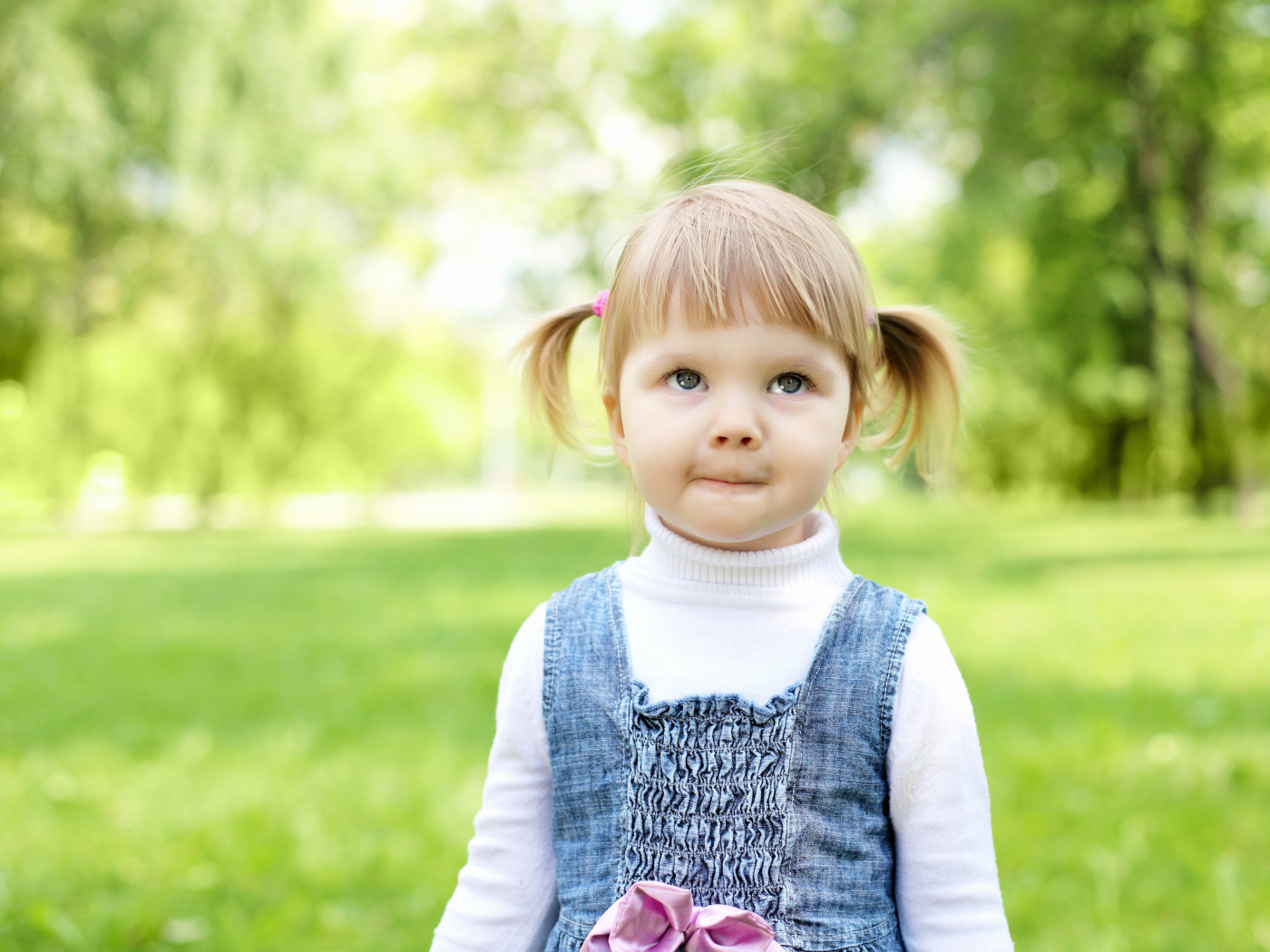 Маленькая девочка с хвостиками на голове в парке 