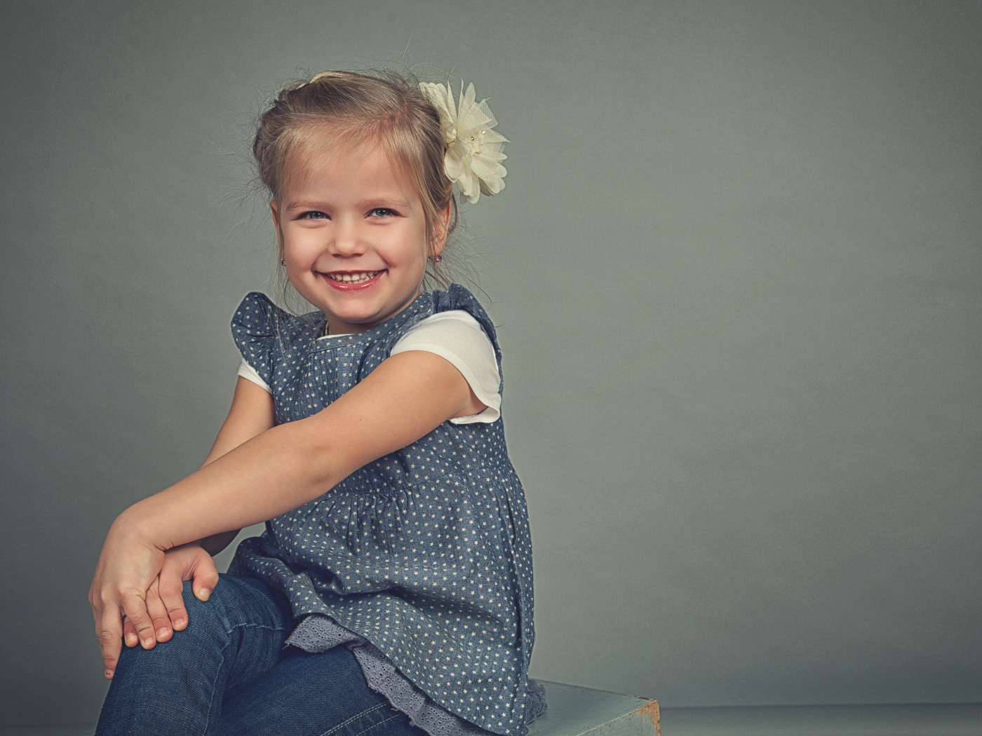 Маленькая улыбающаяся девочка с бантом на сером фоне 