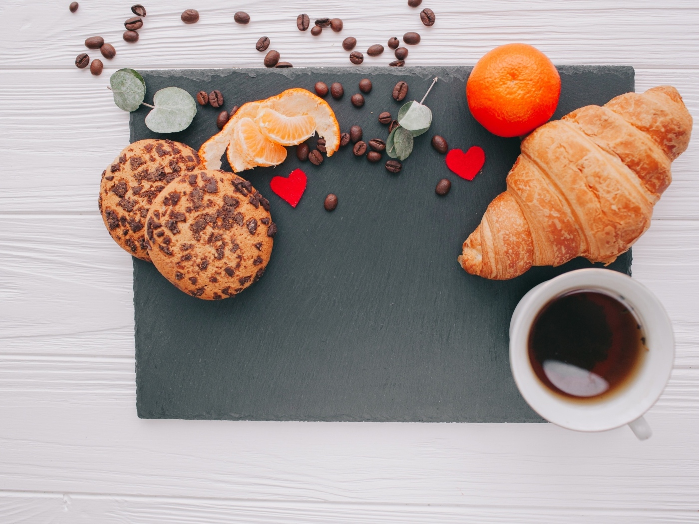 Круассан на столе с печенье, чашкой кофе и мандарином