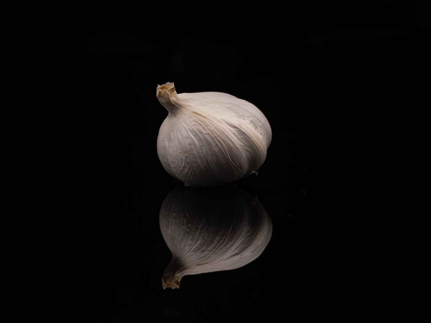 Белый чеснок отражается в черной зеркальной поверхности 