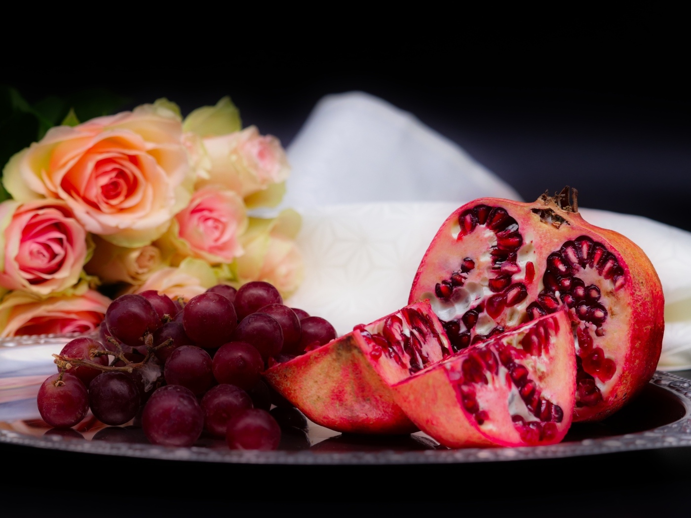 Гранат с виноградом на столе с букетом роз 
