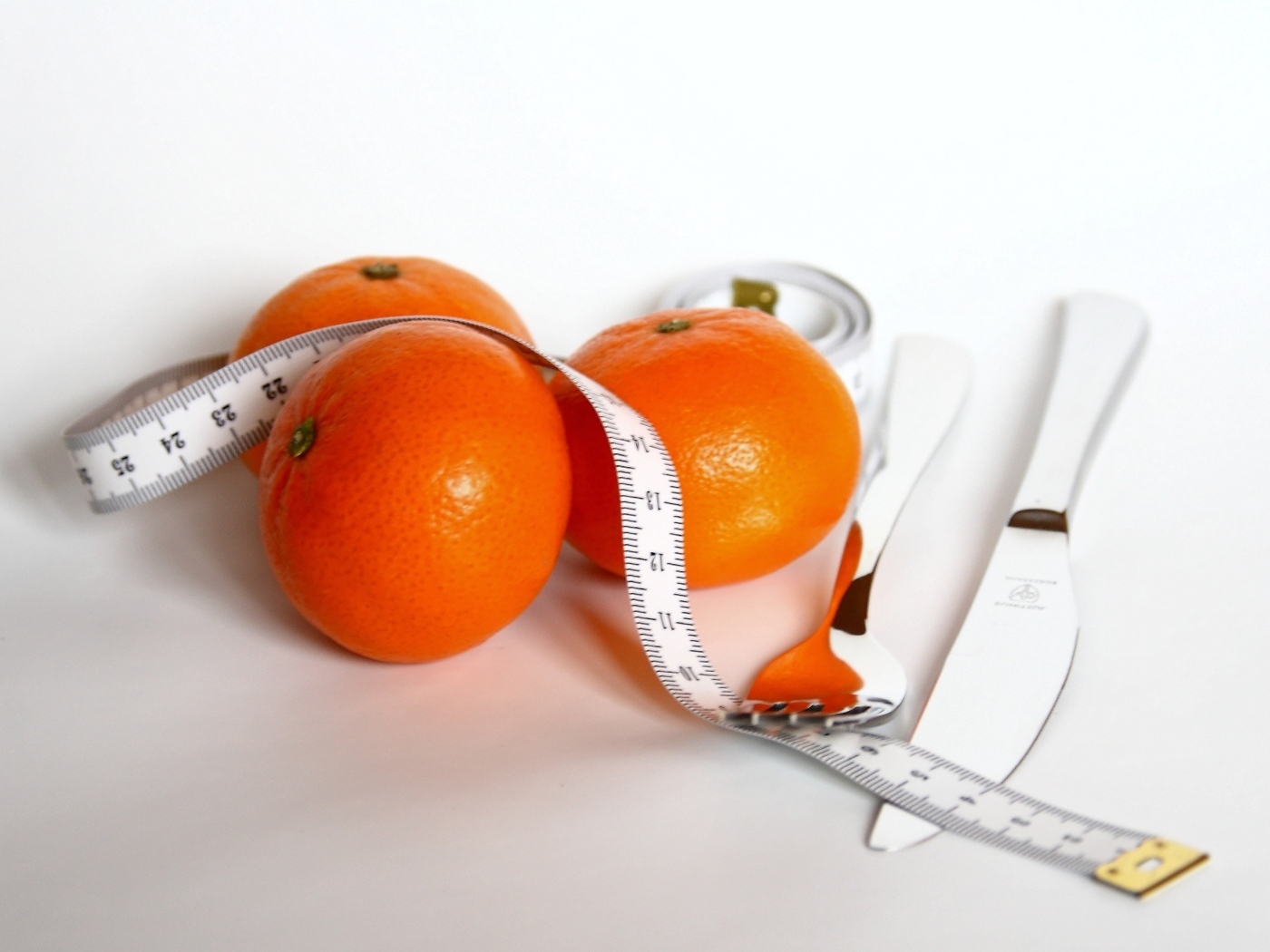 Мандарины с сантиметром и столовыми приборами на белом фоне